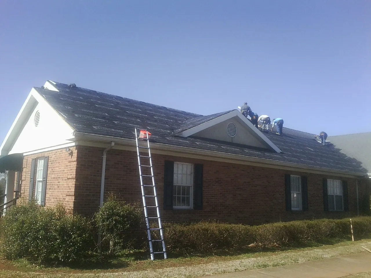 Crew tearing shingles off a brick ranch roof with a ladder set — Emergency Roof Repair work by our crew in Fox Lake