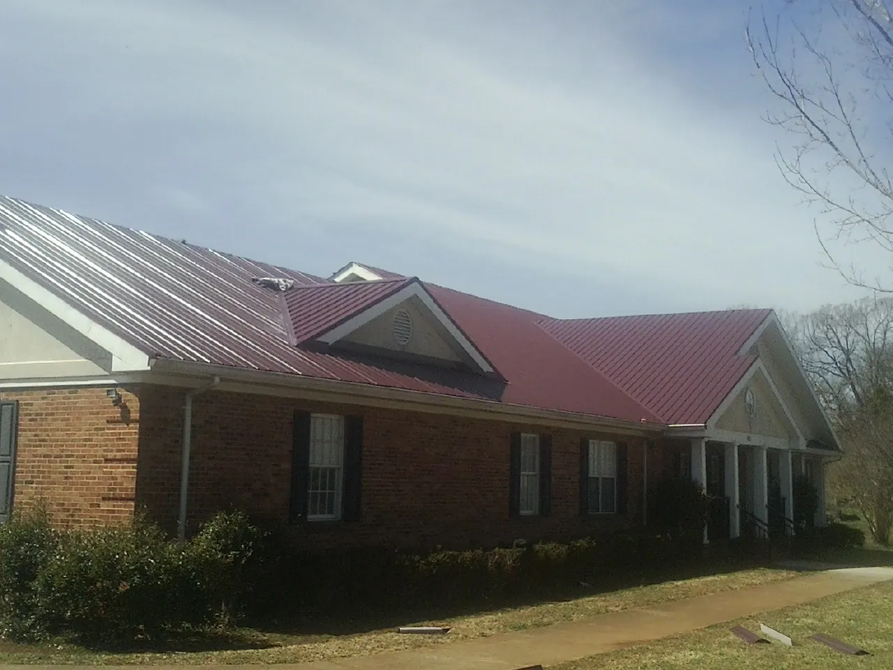 Red metal roof with gabled entries on a long brick building, from a Hail Damage Roof Repair job in Fox Lake