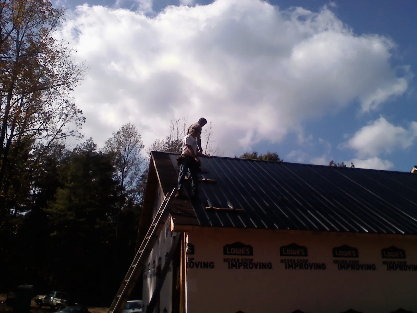 Roofer fastening dark metal panels high against a cloudy sky, from a Roof Inspection job in Fox Lake